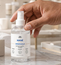 A hand holds a clear bottle of MANÉ Werksvelle Witch Hazel Toner on a marble countertop beside an open gift box, with promotional text in the background.
